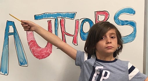 third grade student at Almost Authors points to welcome sign on whiteboard with pencil