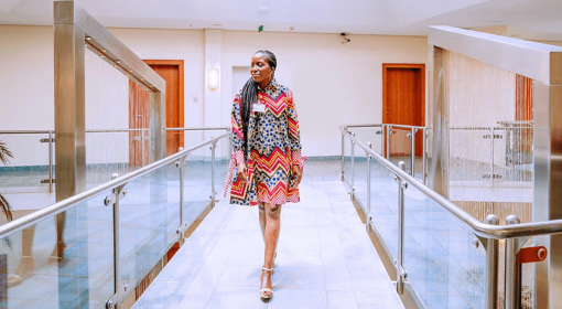 Black African woman wearing print dress and walking in glass-paned, sunlit hallway