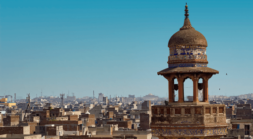 Spire of mosque against the blue sky, with tan-and-brown cityscape in background