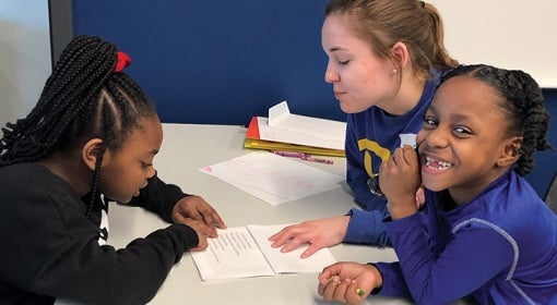 A pitt student tutors two little kids in reading at a table with paper and crayons