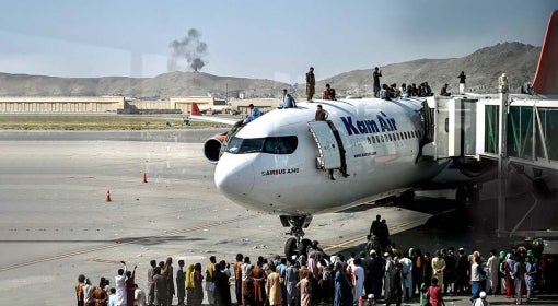 a crowd of people stands on tarmac and on top of Kam Air airplane in Kabul