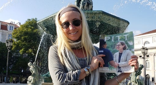 blonde woman sits on edge of fountain holding Winter 2020 issue of Pitt Magazine (picturing Provost Ann Cudd)