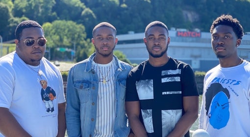 four young Black men stand in sunshine and look at camera