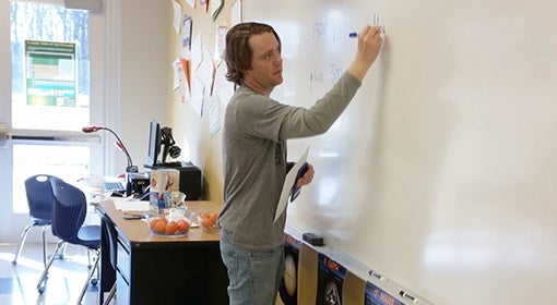 Andrew Van Fossen writes on a whiteboard in a classroom.