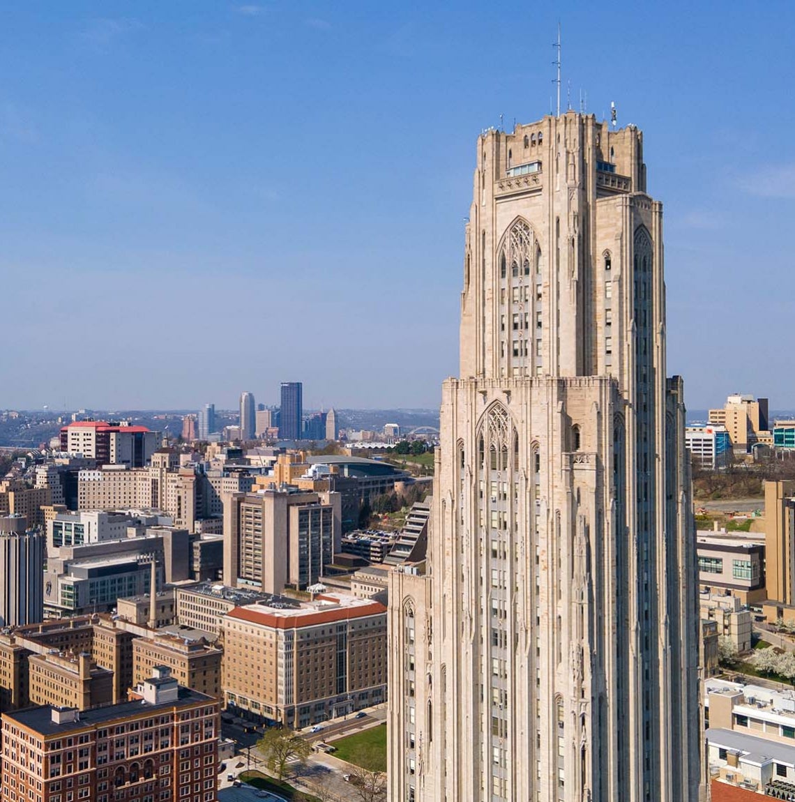 Drone-shot image of the Cathedral of Learning with Oakland and Downtown Pittsburgh in background
