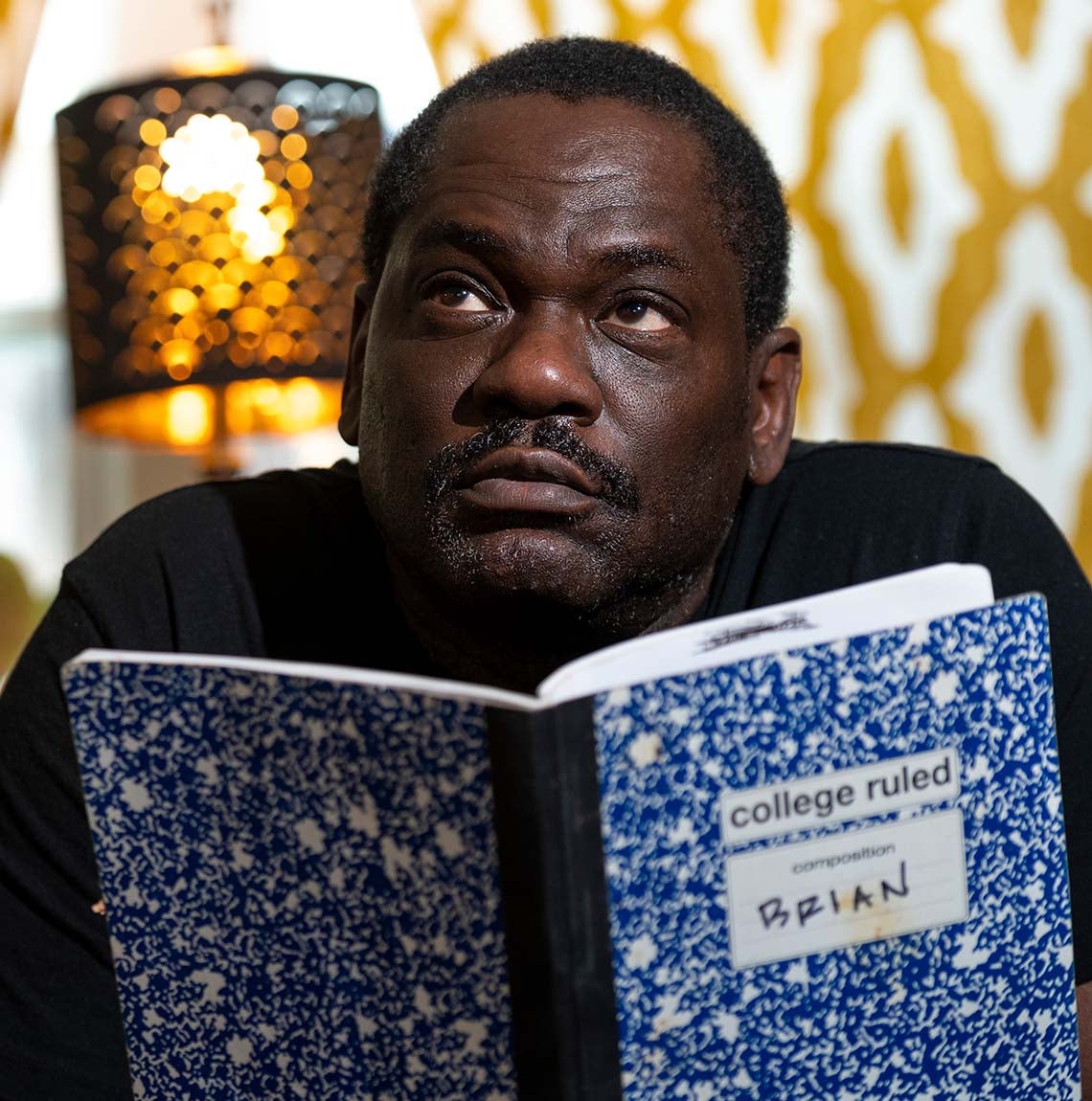 Black man holds up blue-marbled, college ruled composition book with "BRIAN" written in black on front