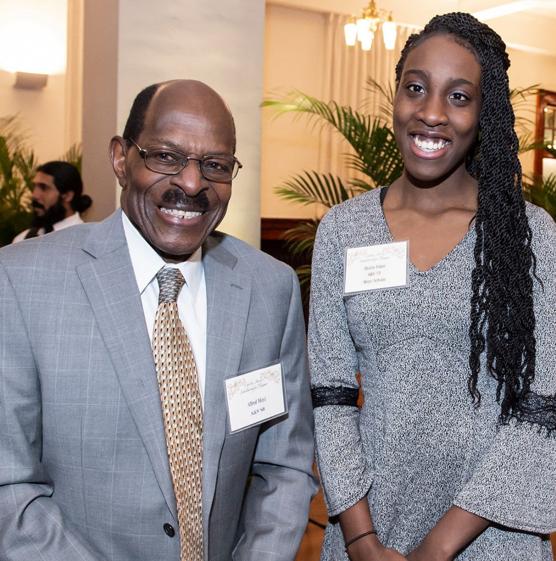 man in gray suit with tie and young woman in gray dress stand for photo in ballroom