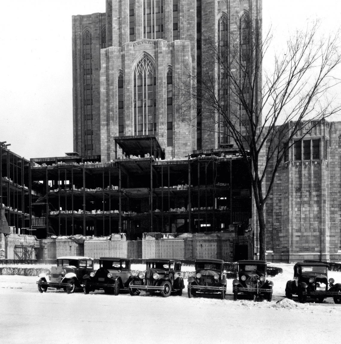 black and white photo of Cathedral with side under construction, old cars lined up in snow in front of it