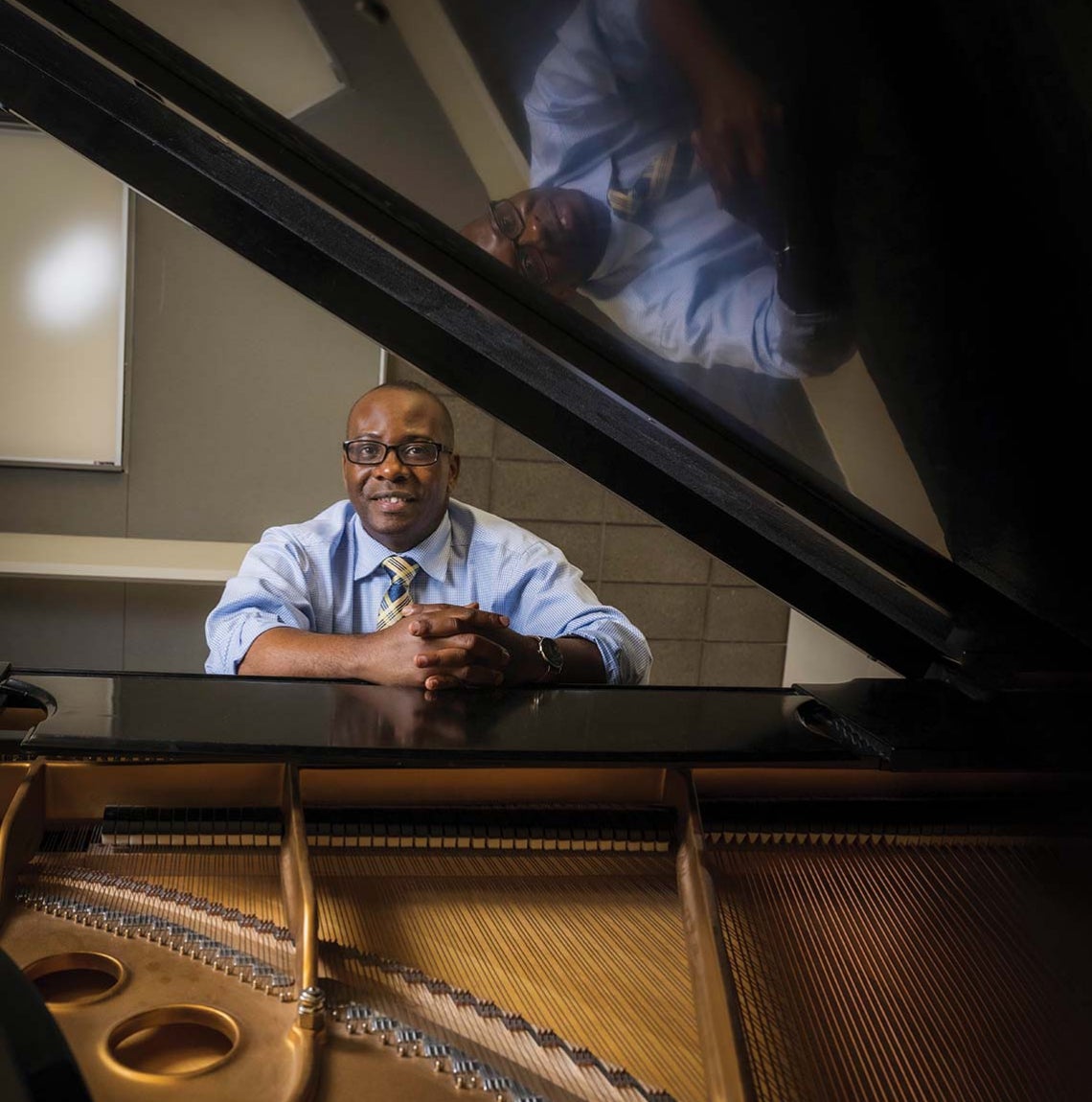 man sits at bench of grand piano, with a view of piano's interior