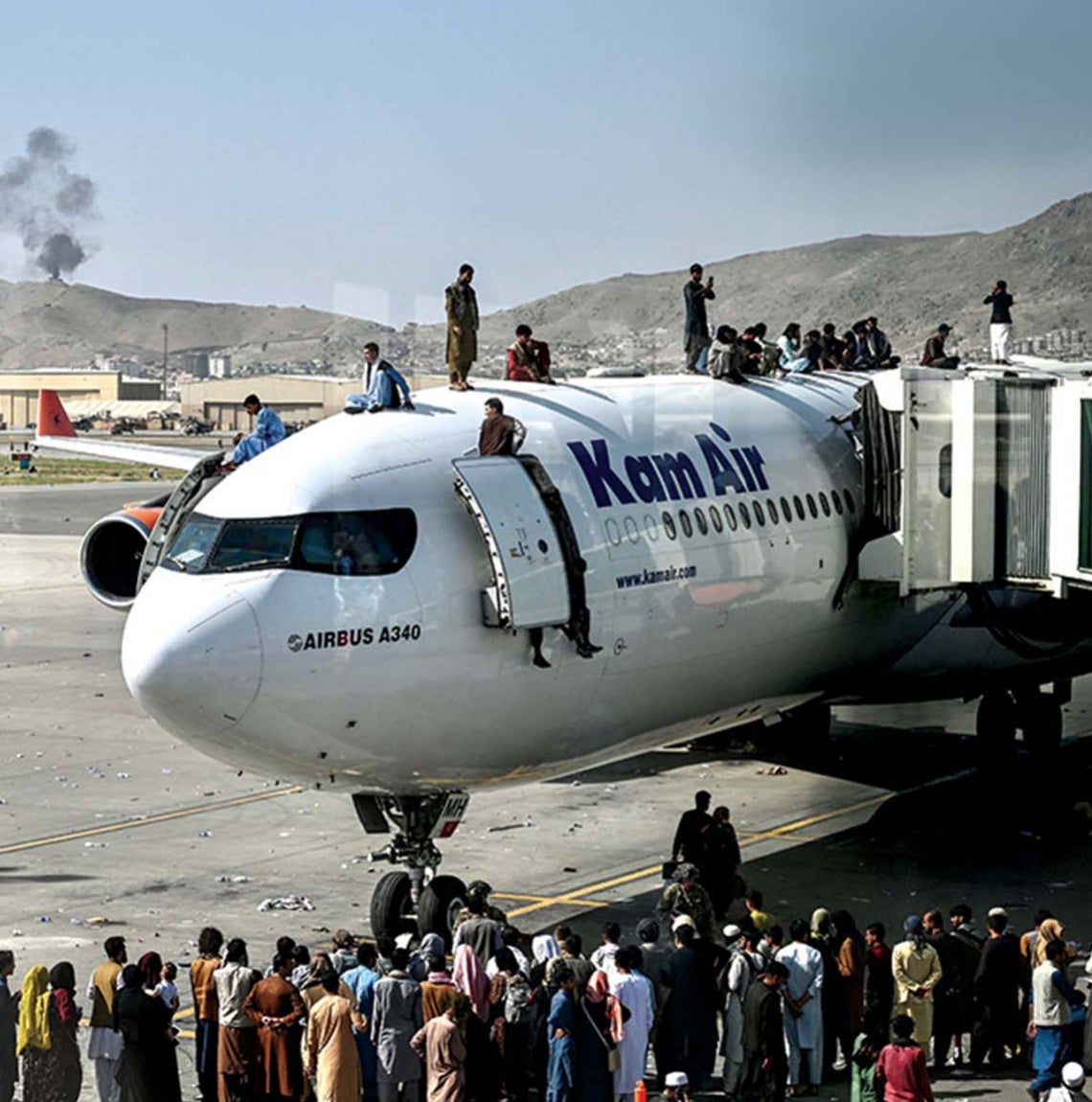 a crowd of people stands on tarmac and on top of Kam Air airplane in Kabul