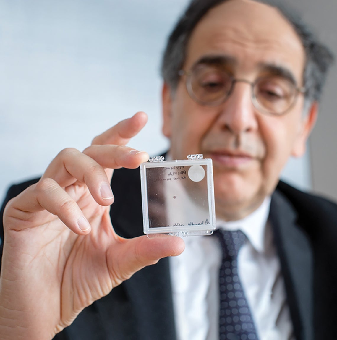 main in dark suit holds glass slide in focus for camera