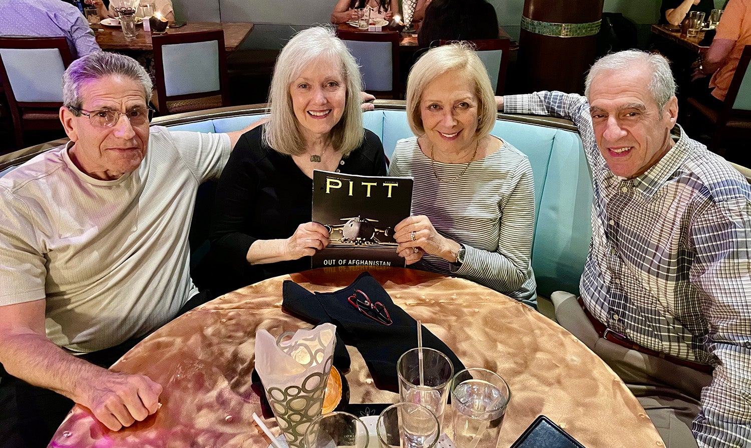 Four people sit around a magazine at a restaurant booth